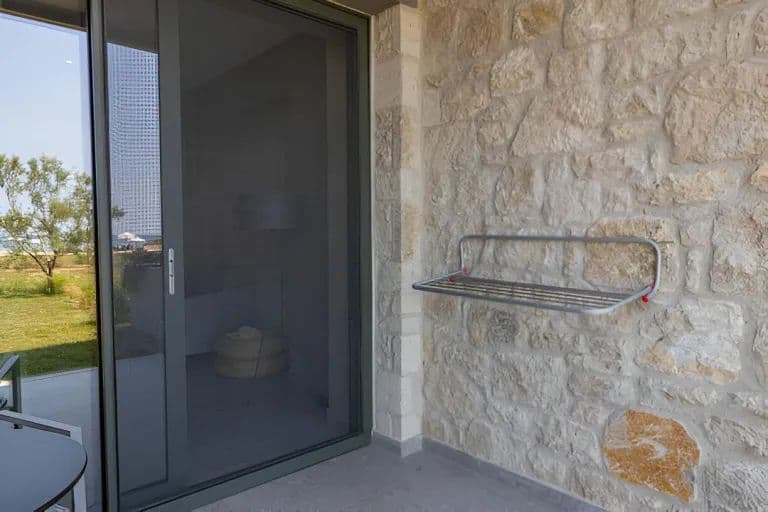 Zanzariera scorrevole su portafinestra, accanto a una parete in pietra a vista
